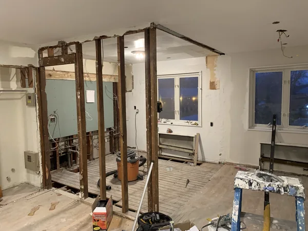 Demolition of the dividing wall between the living room and kitchen in Bayside, with studs exposed and the old drywall stripped away