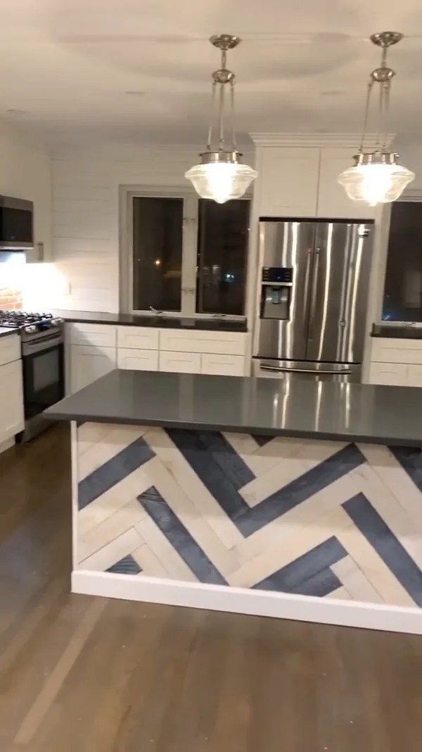 The finished island with two-tone herringbone wood cladding, dark quartz countertop and pendant lights