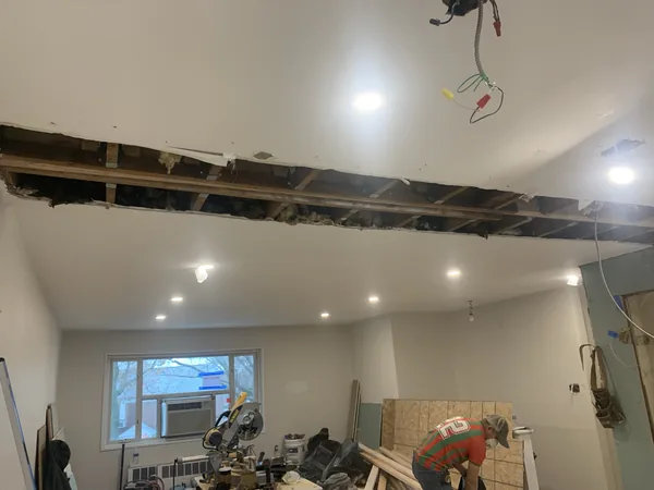 The opened Bayside kitchen and living space during rough-in, with recessed lighting wired in and the recessed ceiling beam channel visible