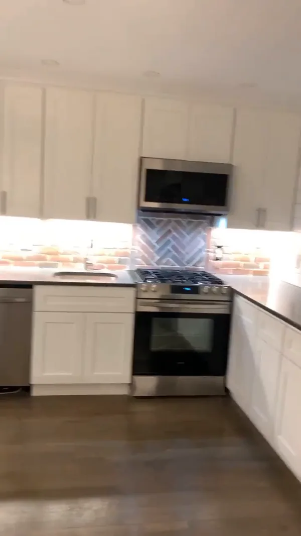The white shaker cabinet run with gas range, hood and herringbone tile backsplash accent