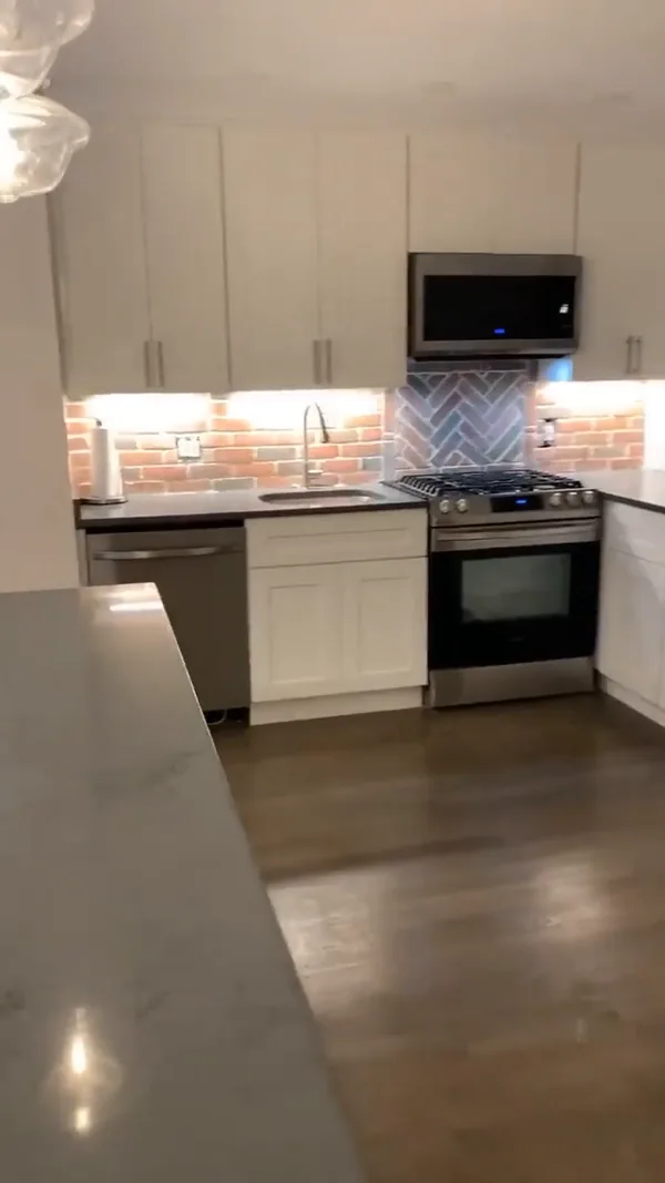 The finished sink run with brick backsplash, gooseneck faucet and under-cabinet LED lighting