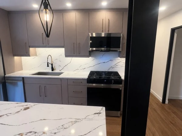 View past the dark finished beam into the new open kitchen with the quartz island in the foreground