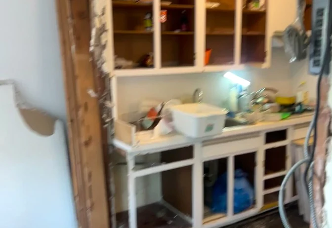 The old Bayside kitchen run with worn painted open shelving and cluttered countertops before demolition