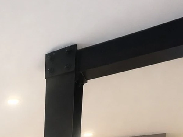 Close-up of the bolted steel beam and post, finished dark and deliberately left in view in the finished kitchen