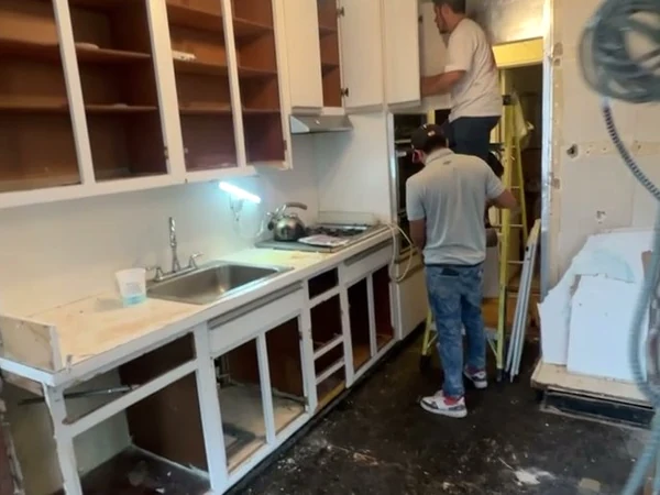 The original enclosed Bayside apartment kitchen with built-in painted shelving, worn countertops and a single dated ceiling fixture