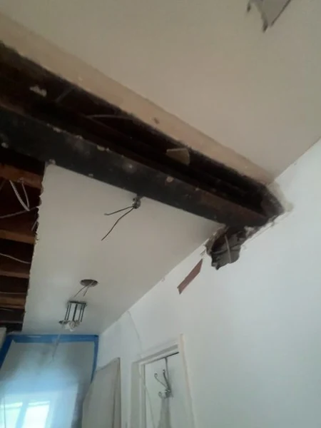 The finished dark beam spanning the expanded opening and carrying the load in place of the removed dividing wall