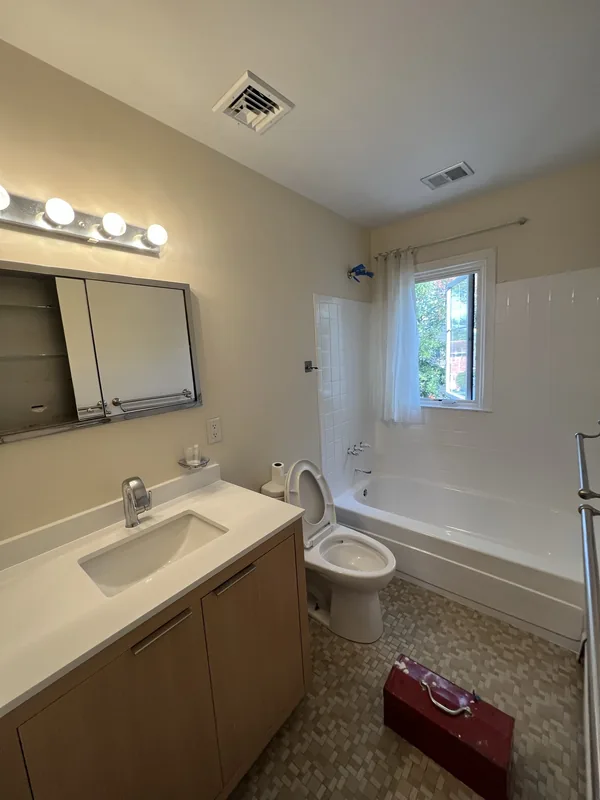The original bathroom vanity with a Hollywood strip light, frameless mirror and beige countertone before the Great Neck remodel