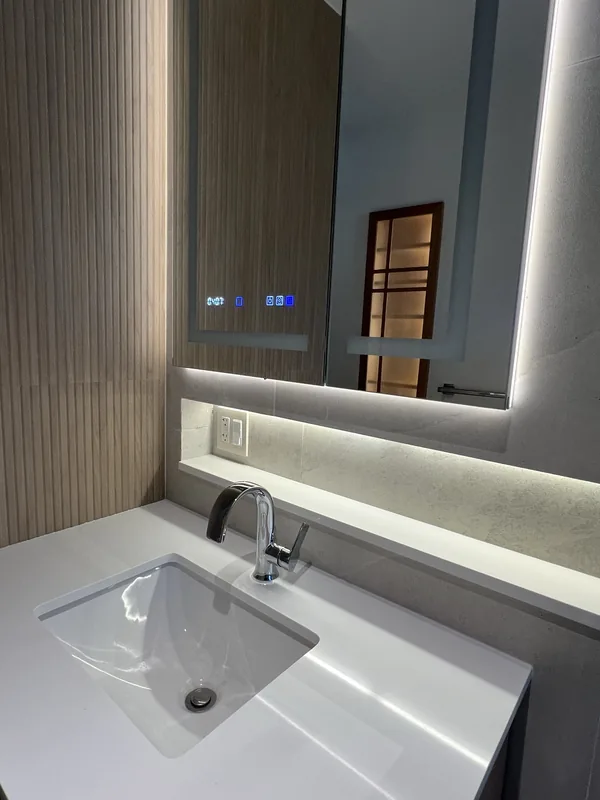 Vanity detail with the fluted wood wall, LED-backlit mirror reflecting the shoji cabinet, and integrated stone sink