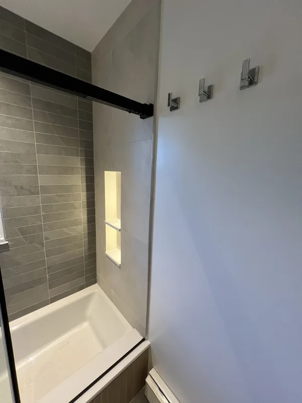 Detail of the LED-illuminated shower niche in gray porcelain tile beside the tub