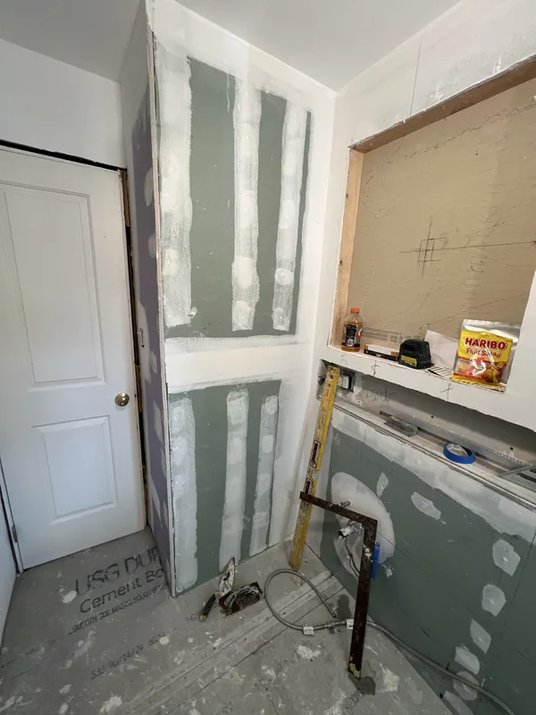 The bathroom entry wall at rough-in with taped drywall, rough plumbing and cement board floor before tiling