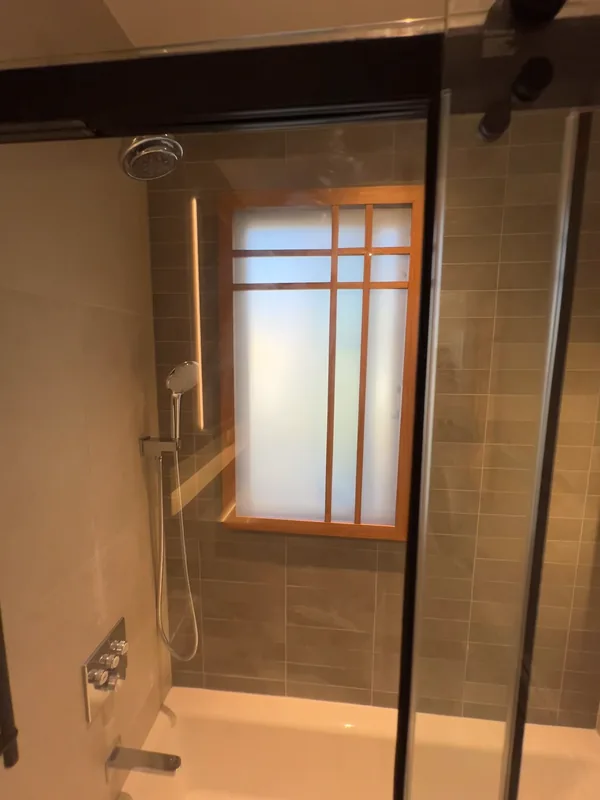 The finished shower seen through the bypass glass, with chrome fixtures on a slide bar and the shoji screen over the window