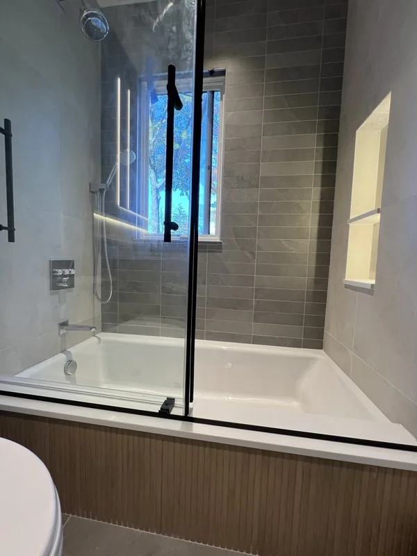 The finished soaking tub and shower enclosure with the custom shoji screen over the window and fluted wood tub apron