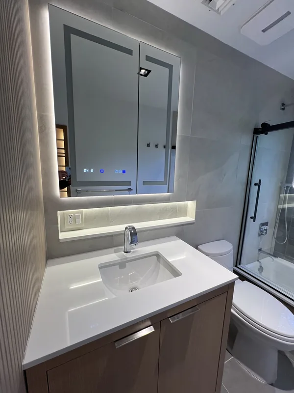 Vanity with under-cabinet cove lighting, large-format gray tile and the bypass glass shower enclosure in the finished Great Neck bathroom