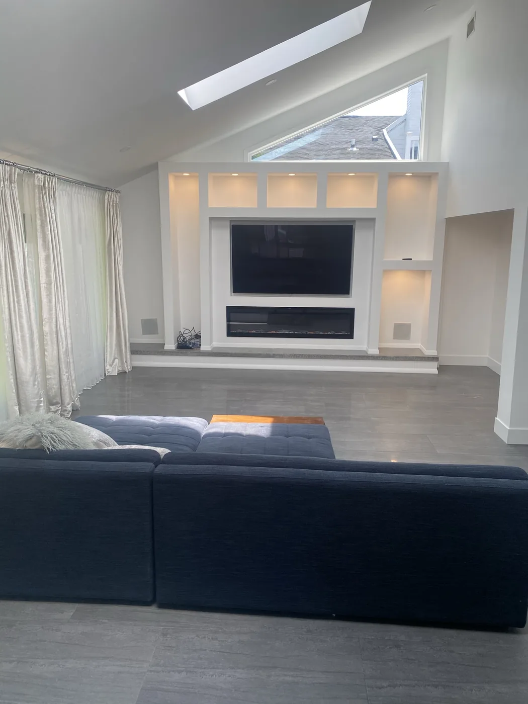 Kings Point media wall finished — recessed television, linear fireplace and cove lighting under a vaulted ceiling