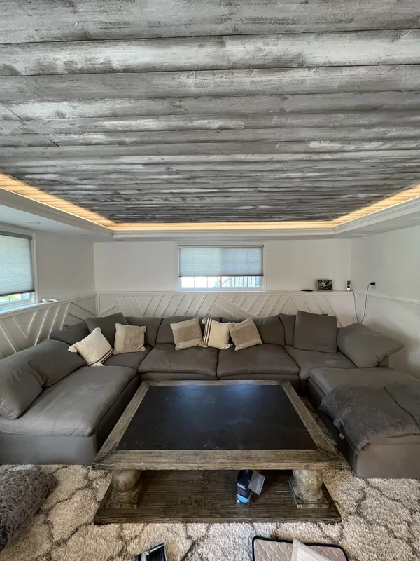 The finished Malba family room, furnished, with white geometric millwork and wood tray ceiling.