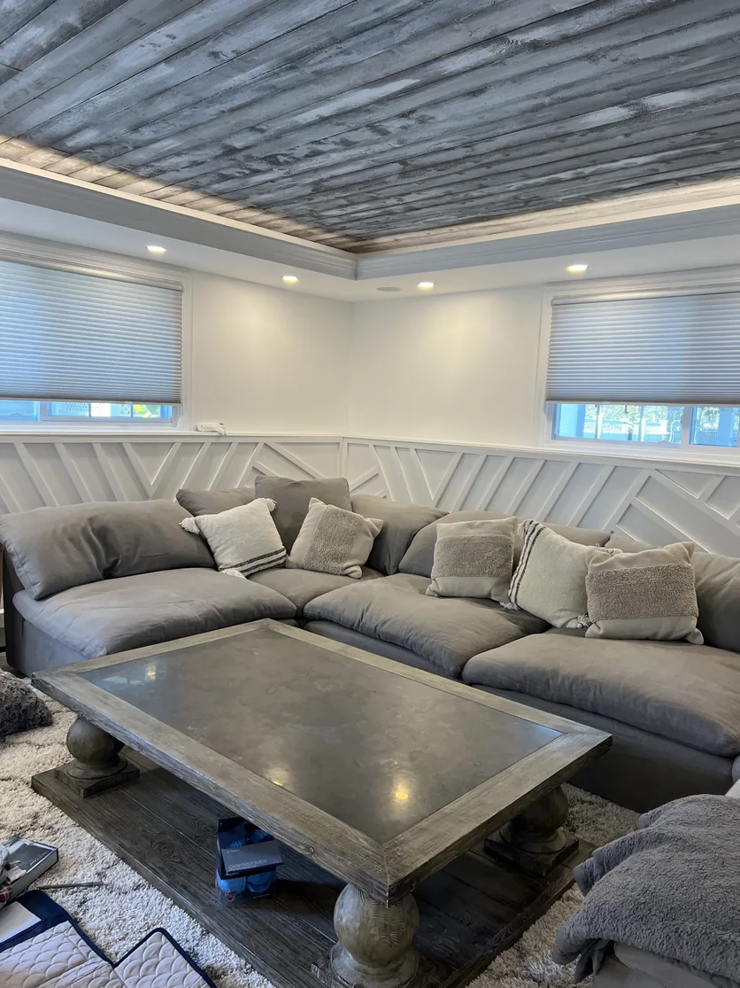 Wide view of the furnished Malba family room with the sectional, geometric millwork and wood tray ceiling.
