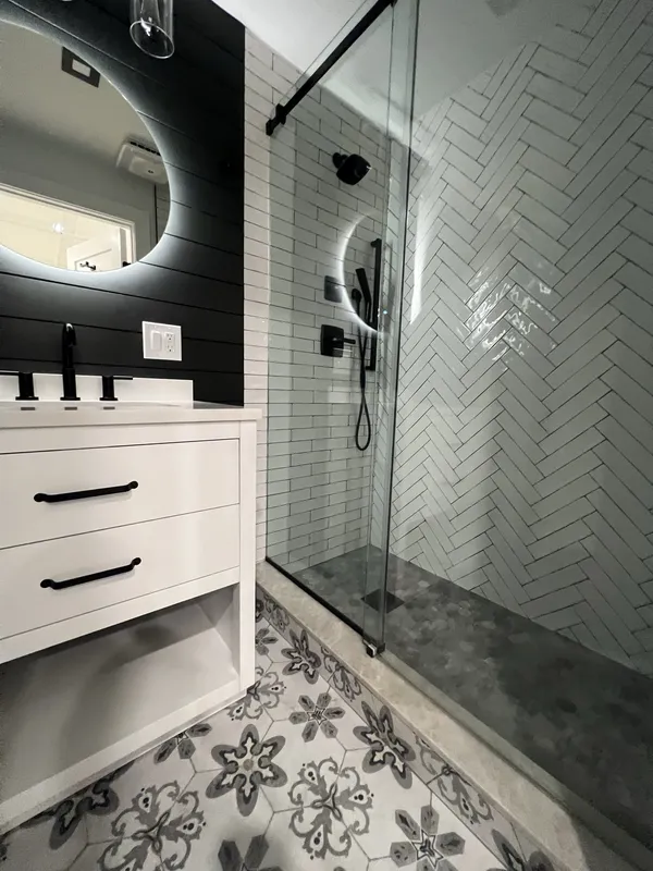 Shower detail: matte-black rain head, handheld slide bar and valve trim against herringbone subway tile.