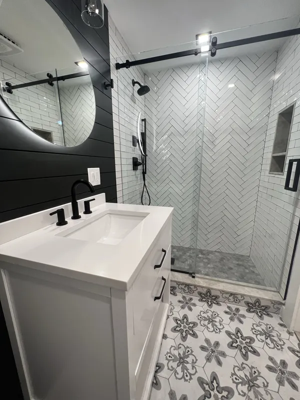 The white vanity with open shelf, quartz top, matte-black widespread faucet and pulls, shiplap behind.