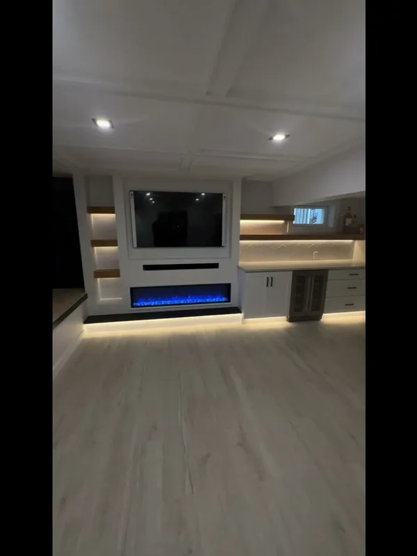 The finished media wall from the room, TV mounted, fireplace glowing blue, wet bar to the right.