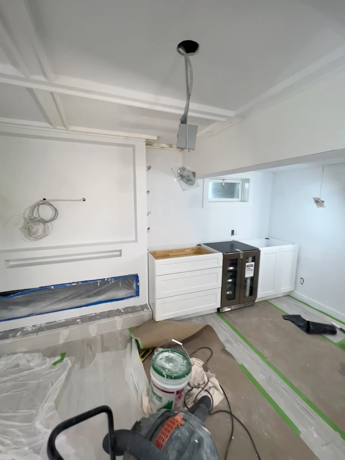 The same room mid-build: framing done, TV wall taped off for the fireplace aperture, wet-bar cabinets set, wine fridge in place.