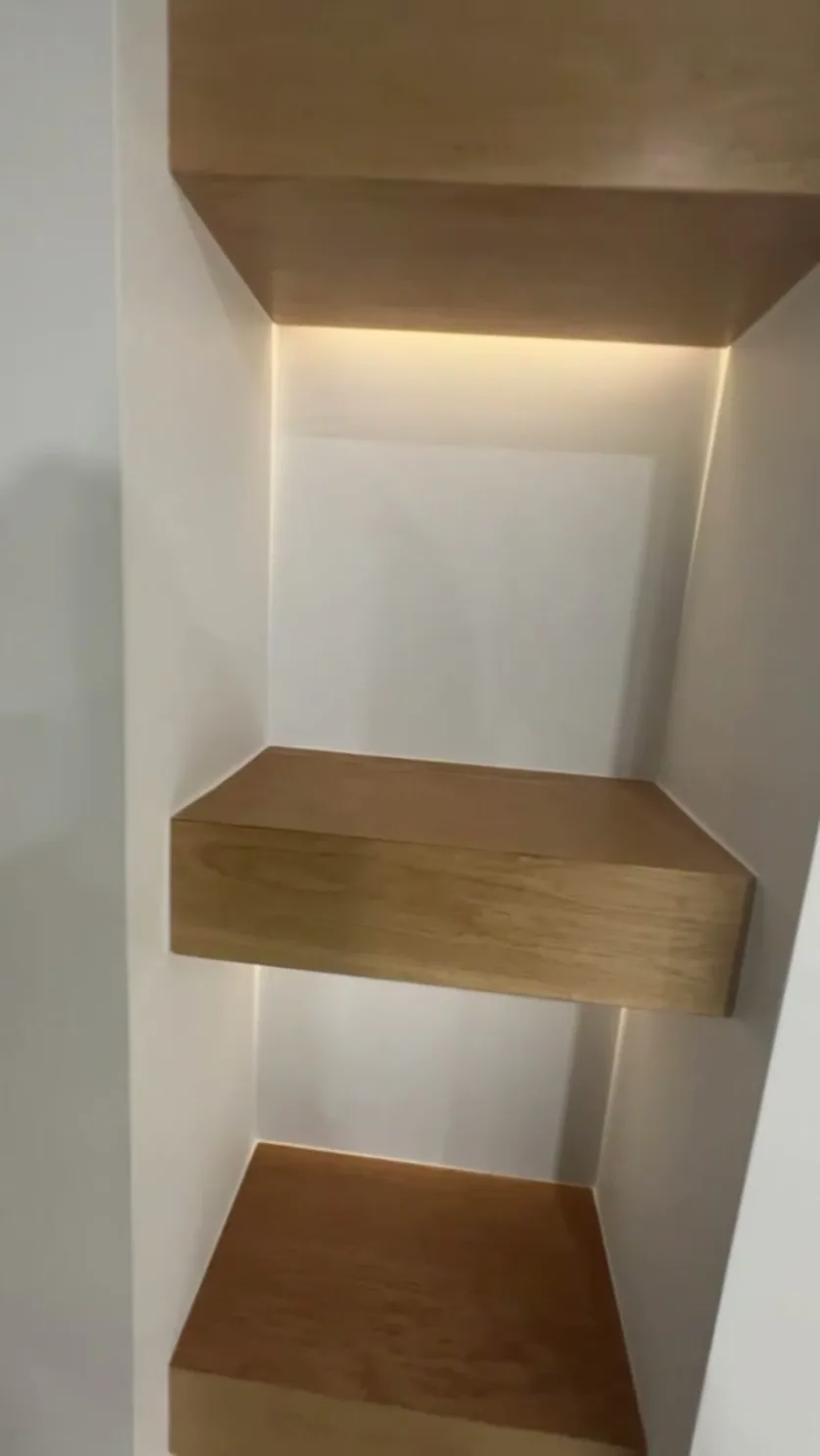 Floating white-oak shelves in the media niche, back-lit with a warm LED cove.