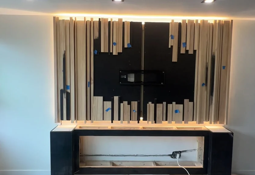 The Malba media wall mid-build, with bare cedar slats set against a blacked-out panel and the console frame open