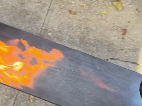 Flames along a charred cedar board on sawhorses, showing the cracked alligator-skin surface forming
