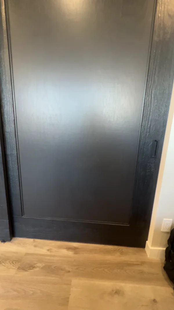 The solid charred cedar bypass closet door with its recessed flush pull, seen straight on above the oak floor