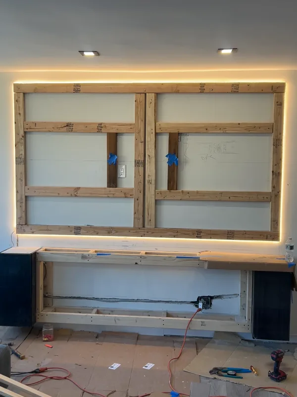 Media wall framing with perimeter blocking and warm LED backlighting during the Malba build