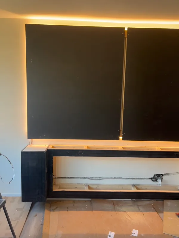 Matte black backer panels installed over the framed media wall with warm halo edge lighting