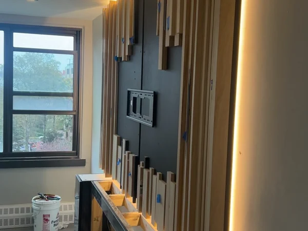 Cedar slats being installed against the blacked-out panel with LED cove lighting already lit