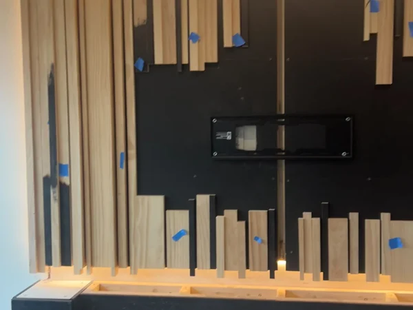 Staggered slat layout and TV mount on the blacked-out substrate during the Malba media wall build