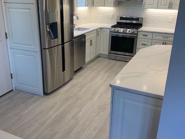 After: view from the entry showing stainless appliances, quartz counters and the tile-to-hardwood threshold