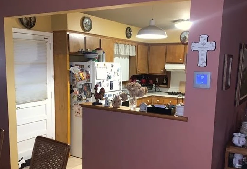 Before: original Whitestone kitchen seen through a narrow half-wall pass-through, with oak cabinets and a mauve dining room wall