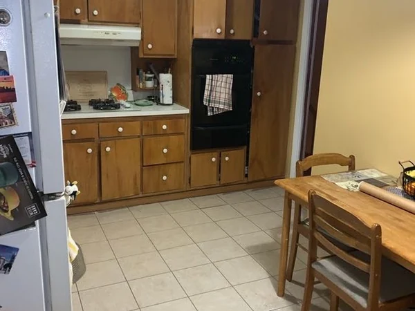 Before: original Whitestone kitchen with oak cabinets, black double wall oven and ceramic tile floor